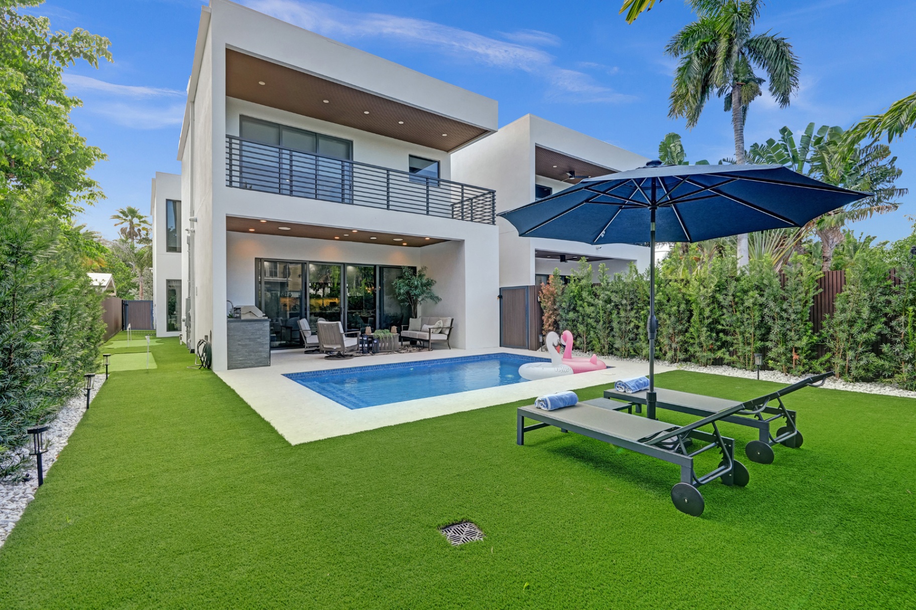Modern two-story rental backyard with pool, lounge chairs, and lush landscaping