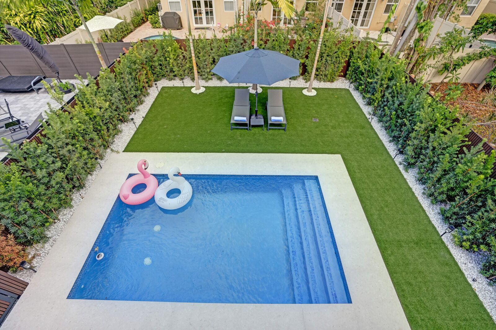 Aerial view of private backyard pool, sun loungers, and manicured lawn